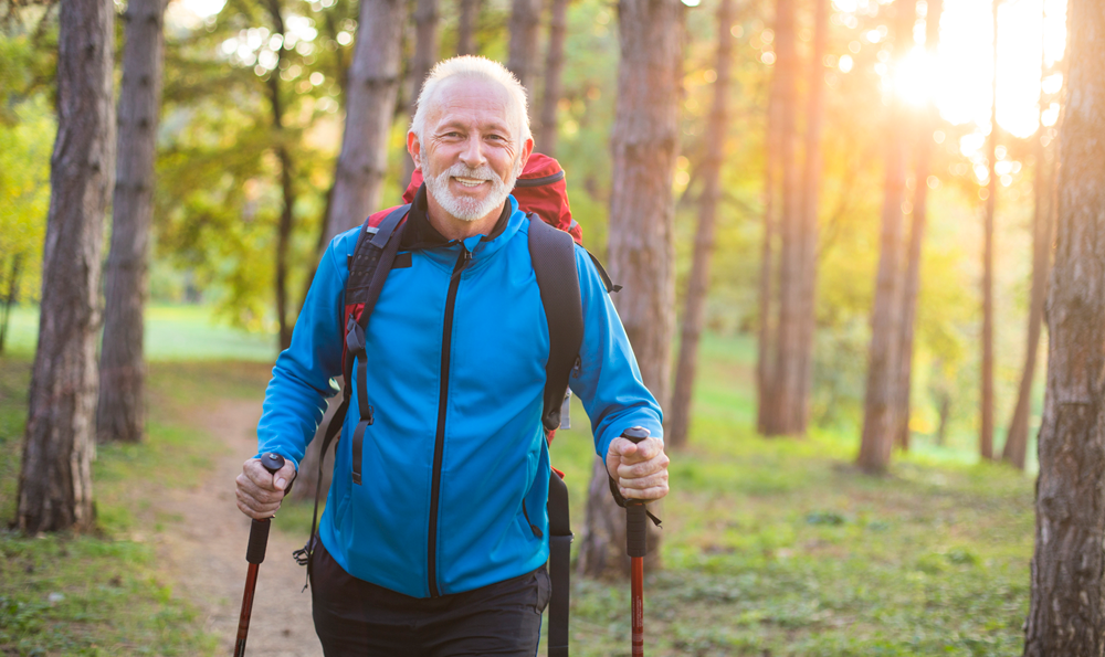 Senior man with arthritis takes a long hike in the forest.