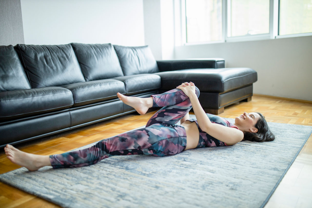 Woman lying and doing Half Knees to Chest Pose at home