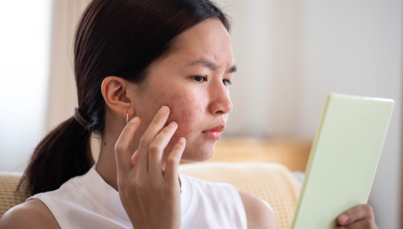 Woman looking at her skin in the mirror.