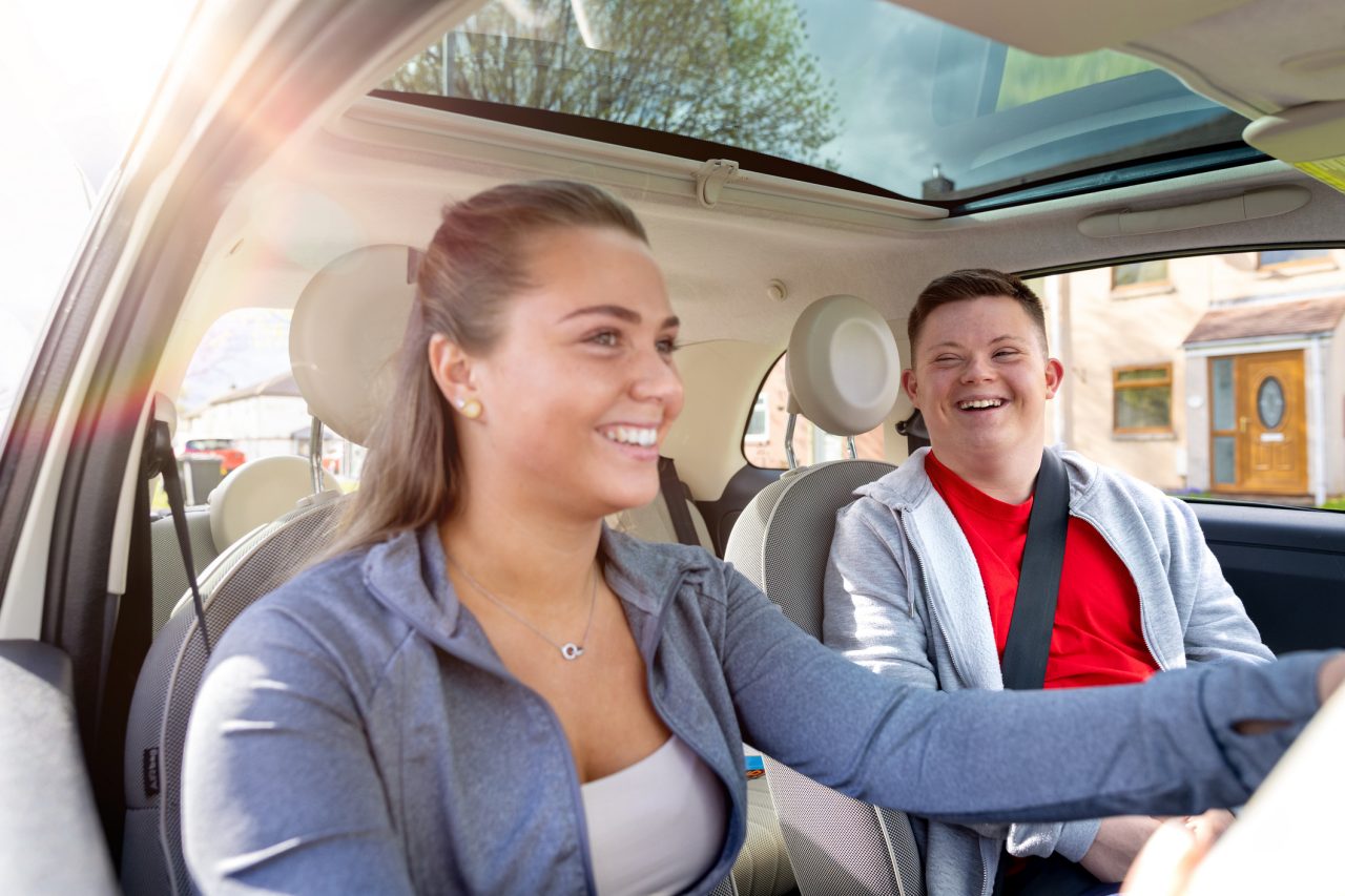 A developmentally disabled young adult rides in a car with his mentor.